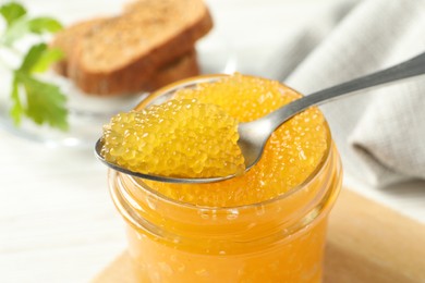 Taking fresh pike caviar from glass jar on white wooden table, closeup