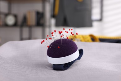 Photo of Pin cushion and grey fabric on table in tailor shop, closeup