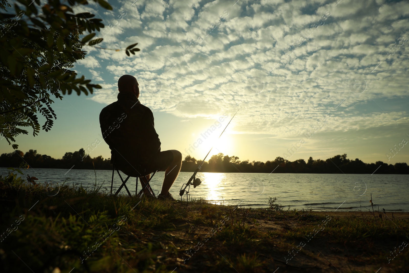 Photo of Fisherman with rod sitting on folding chair and fishing at riverside, space for text