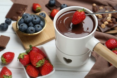 Photo of Dipping fresh strawberry in fondue pot with melted chocolate at white wooden table