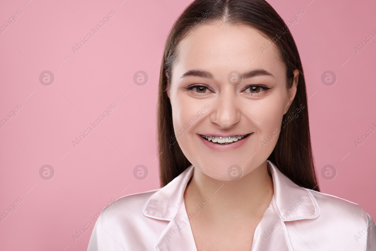 Photo of Smiling woman with dental braces on pink background. Space for text