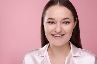 Smiling woman with dental braces on pink background. Space for text