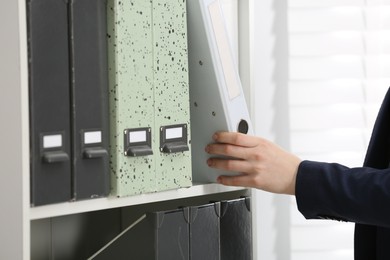 Photo of Woman taking folder with documents from shelf in office, closeup