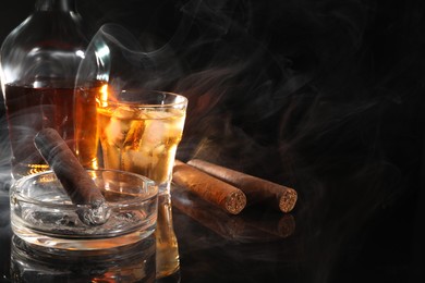 Photo of Smoldering cigar, ashtray and whiskey on black mirror surface. Space for text