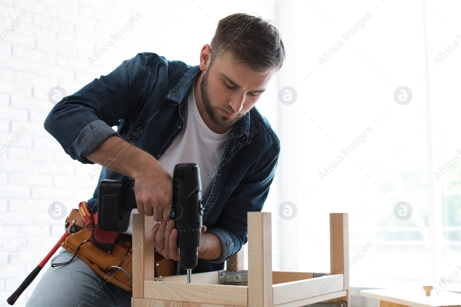 Photo of Young man working with electric screwdriver indoors. Space for text