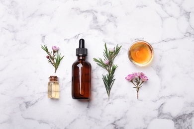 Flat lay composition with bottles of natural tea tree oil on marble table