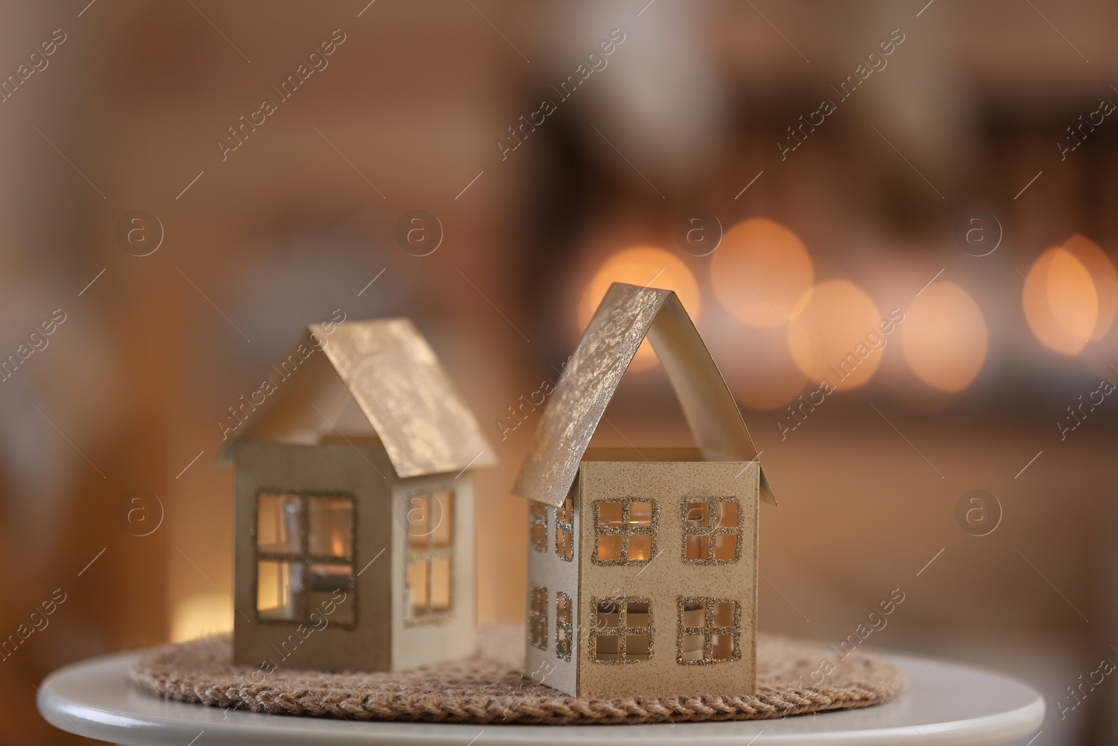 Photo of House shaped candle holders on table against blurred lights. Christmas decoration