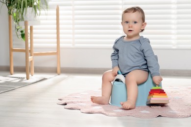 Photo of Little child with toy sitting on plastic baby potty indoors. Space for text