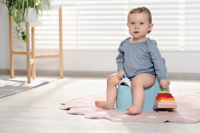 Little child with toy sitting on plastic baby potty indoors. Space for text