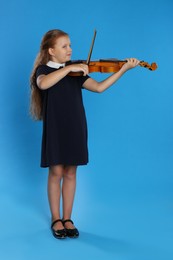 Preteen girl playing violin on light blue background