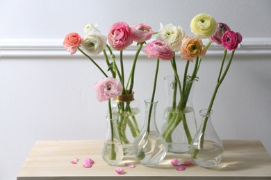 Photo of Beautiful ranunculus flowers on wooden table near wall