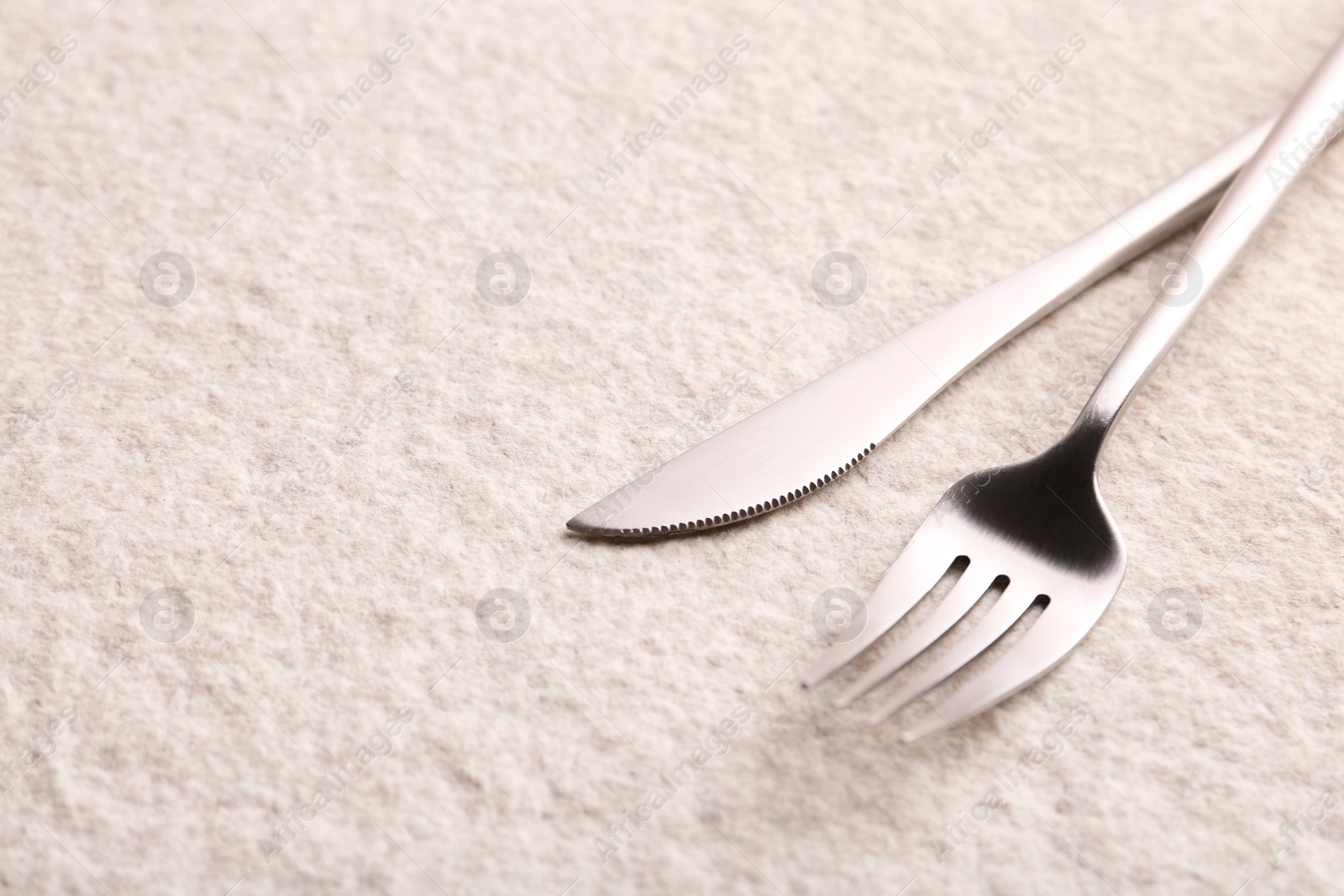 Photo of Stylish cutlery. Silver knife and fork on light textured table, space for text