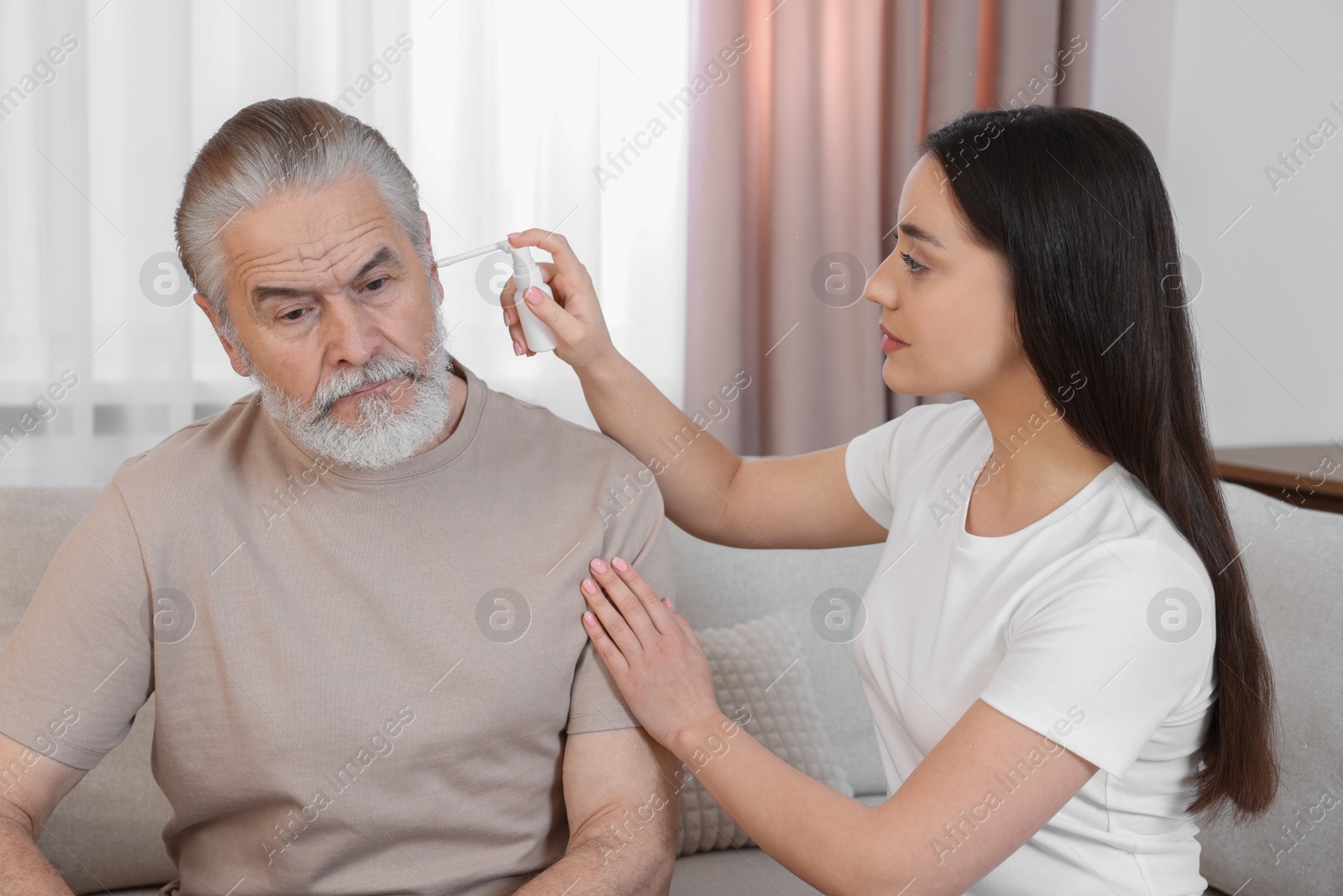 Photo of Young woman spraying medication into man's ear at home