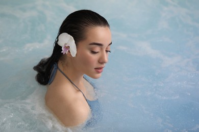 Beautiful woman with orchid flower in spa swimming pool, space for text
