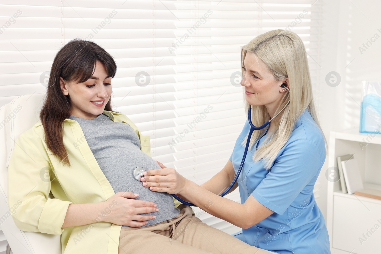 Photo of Pregnancy checkup. Doctor with stethoscope listening baby's heartbeat in patient's tummy in clinic