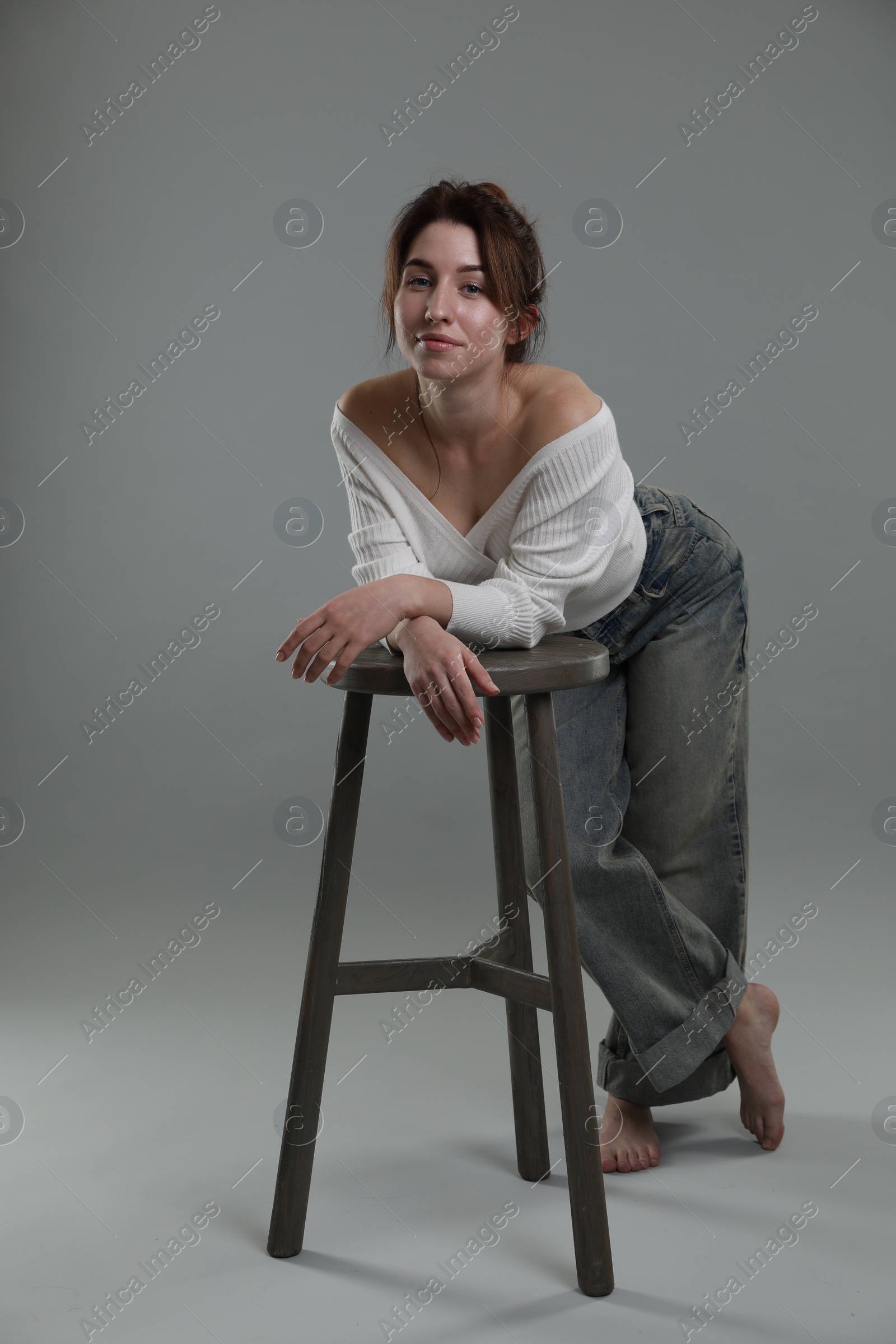 Photo of Beautiful young woman posing near stool on grey background