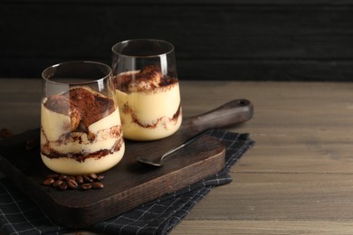 Photo of Delicious tiramisu in glasses, spoon and coffee beans on wooden table. Space for text