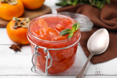 Photo of Jar of tasty persimmon jam and mint on white wooden table, closeup
