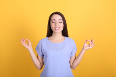 Photo of Young woman meditating on yellow background. Stress relief exercise