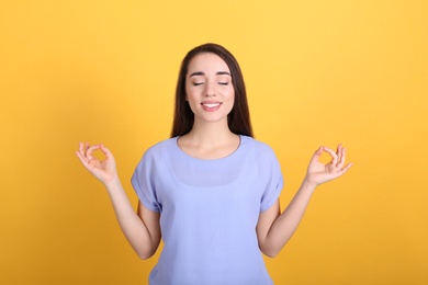 Young woman meditating on yellow background. Stress relief exercise