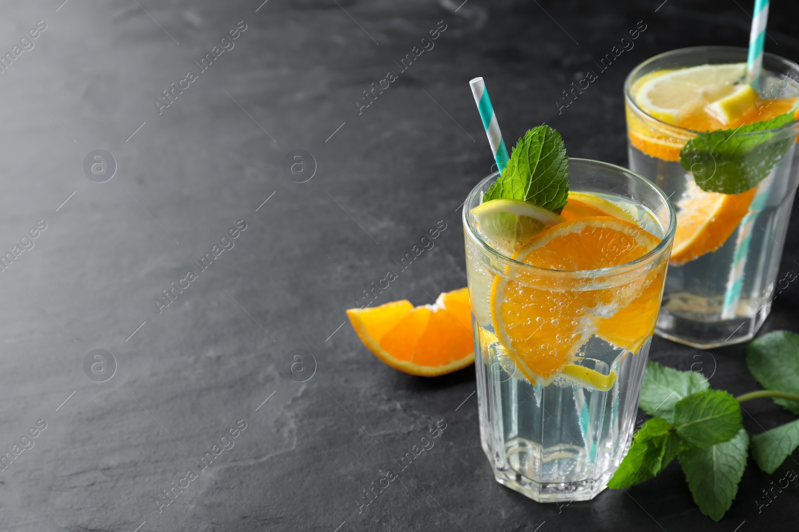 Photo of Delicious orange lemonade with soda water and mint on black table, space for text. Fresh summer cocktail