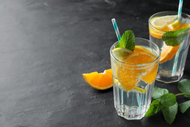 Delicious orange lemonade with soda water and mint on black table, space for text. Fresh summer cocktail