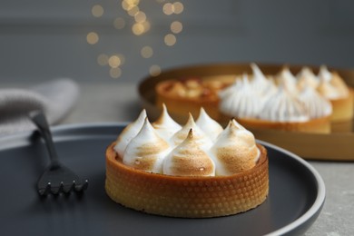Tartlet with meringue on grey table against blurred festive lights, closeup. Delicious dessert