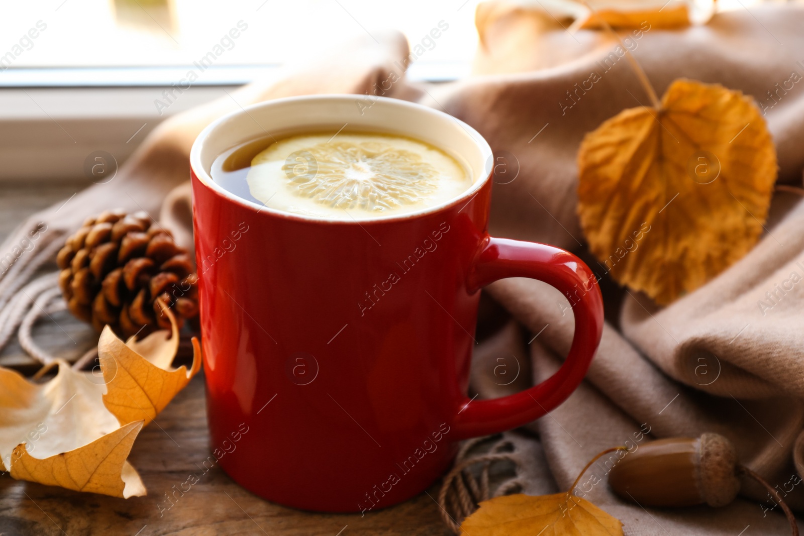 Photo of Cup of hot drink, scarf and autumn leaves on windowsill. Cozy atmosphere