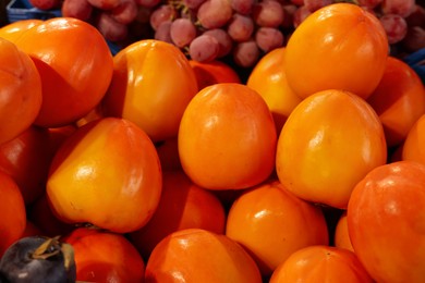 Photo of Many fresh persimmons and grapes on counter, closeup