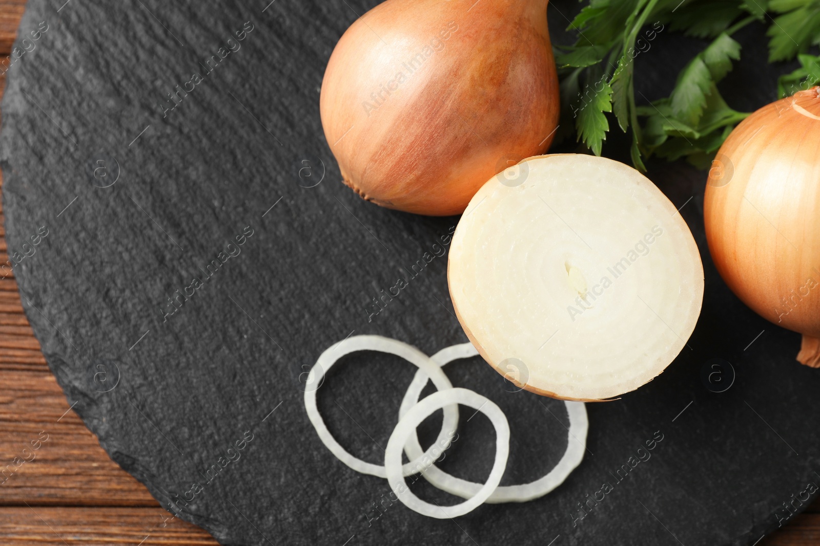 Photo of Whole and cut onions with parsley on wooden table, flat lay. Space for text