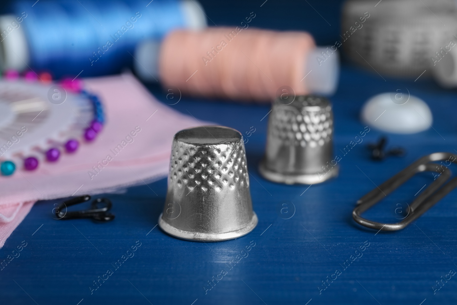 Photo of Silver thimble on blue wooden table, space for text. Sewing accessories