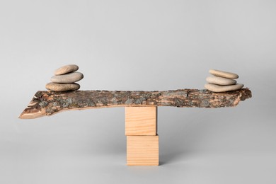 Photo of Stacks of stones balancing on wooden stick against light background. Harmony concept