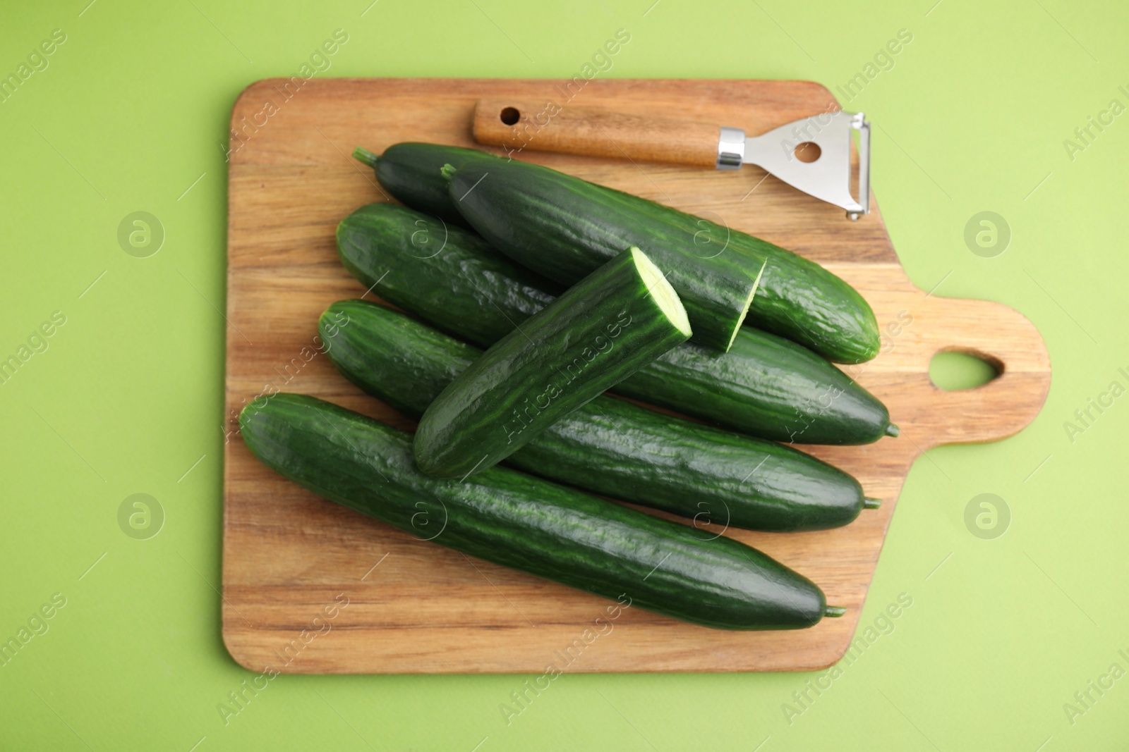 Photo of Fresh cucumbers and peeler on green background, top view