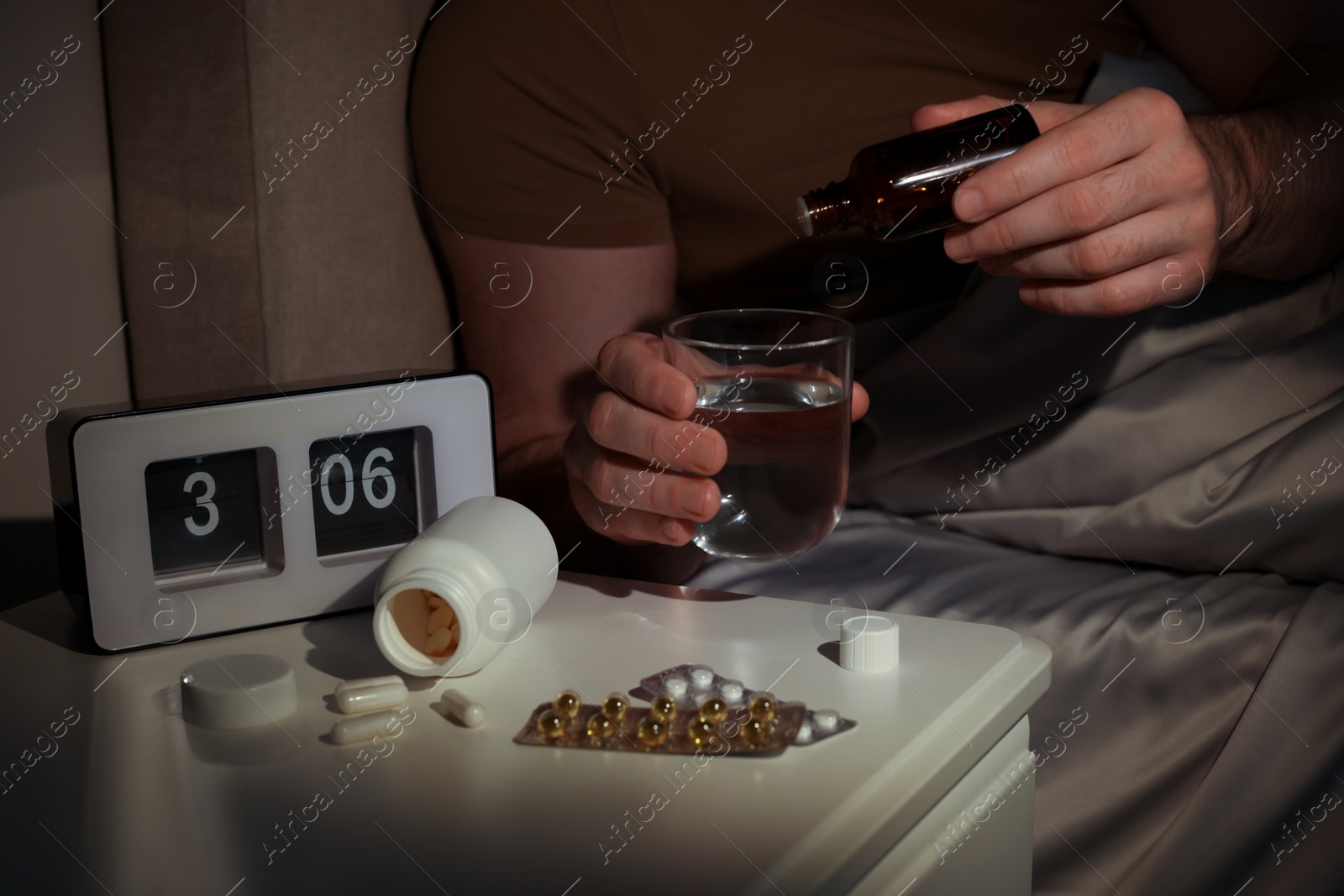 Photo of Man dripping medicine into glass of water in bed at night, closeup. Insomnia concept