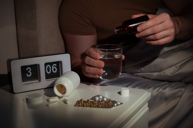 Man dripping medicine into glass of water in bed at night, closeup. Insomnia concept