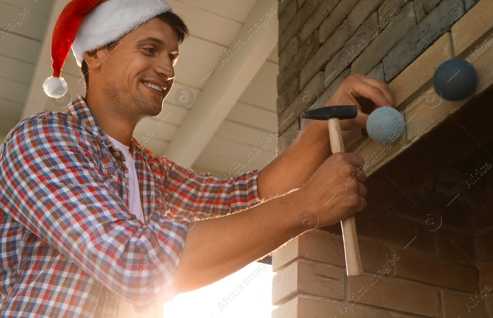 Photo of Man in Santa hat decorating fireplace in house with Christmas lights