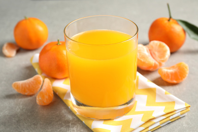 Photo of Glass of fresh tangerine juice and fruits on light grey table