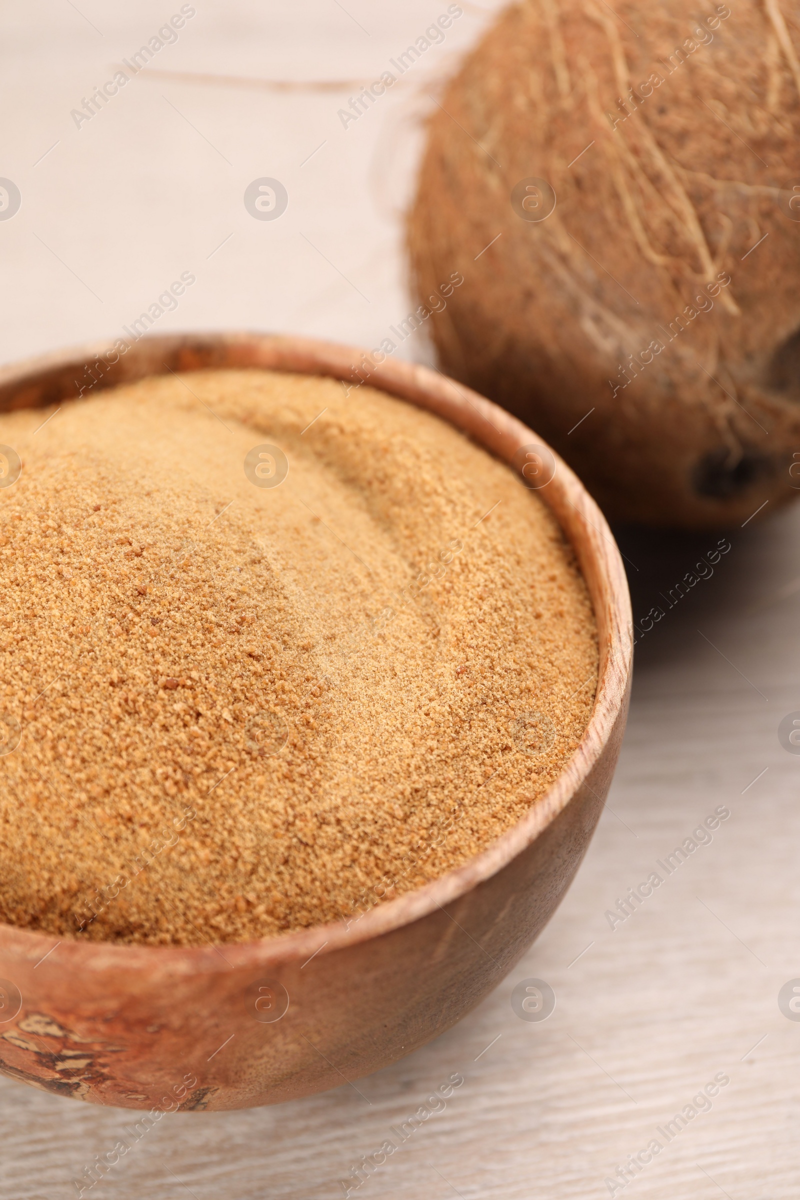 Photo of Coconut sugar in bowl and fruit on light wooden table, closeup