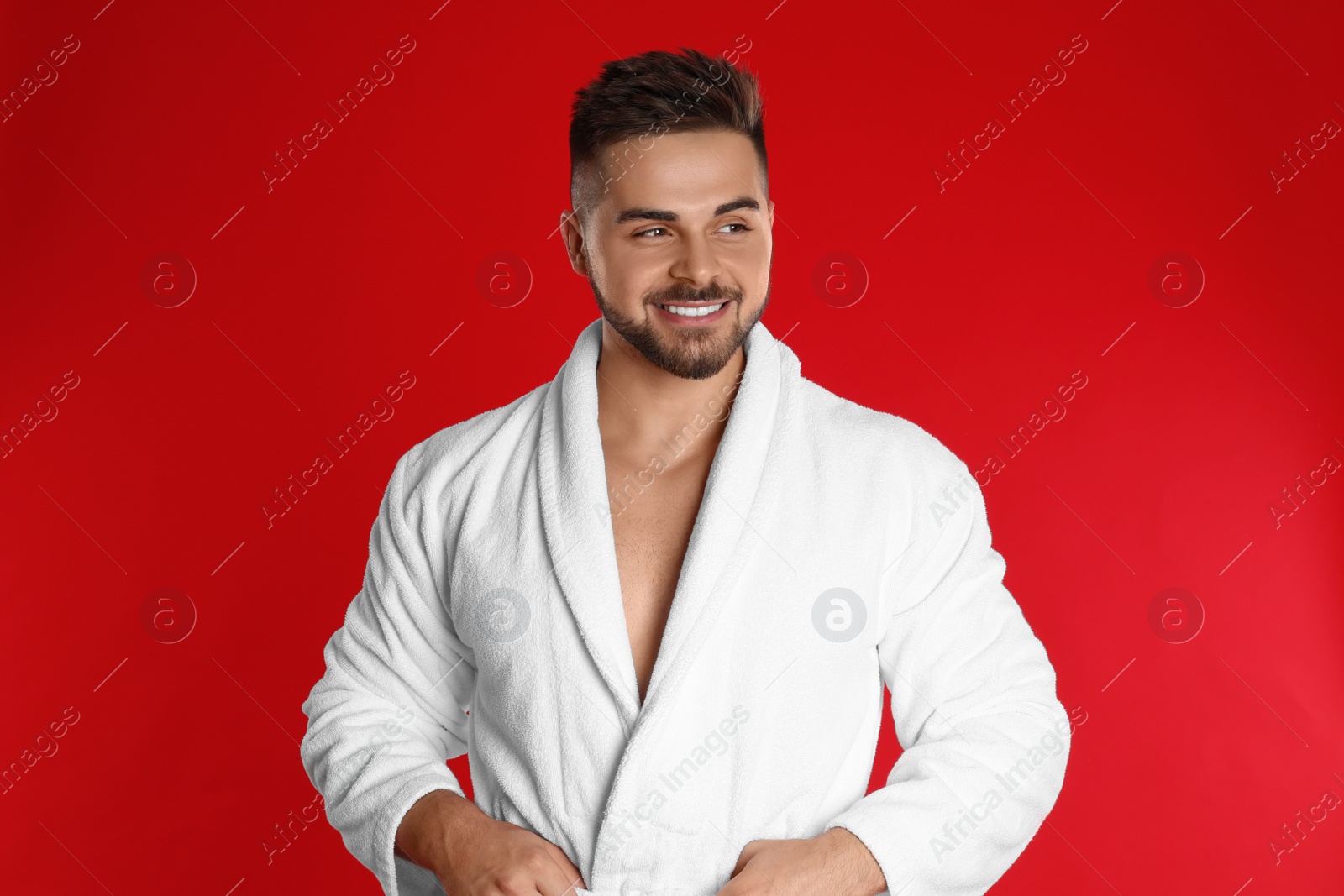 Photo of Happy young man in bathrobe on red background