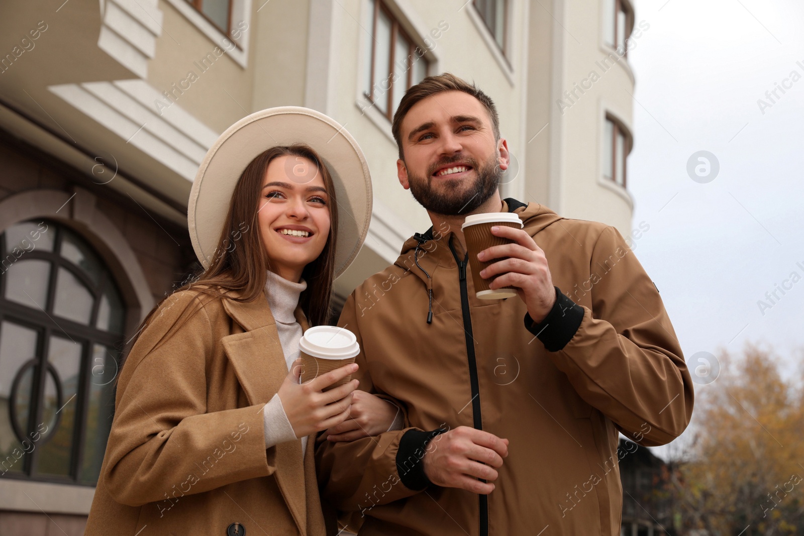 Photo of Happy couple wearing stylish autumn clothes with cups of coffee on city street