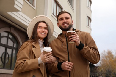 Photo of Happy couple wearing stylish autumn clothes with cups of coffee on city street