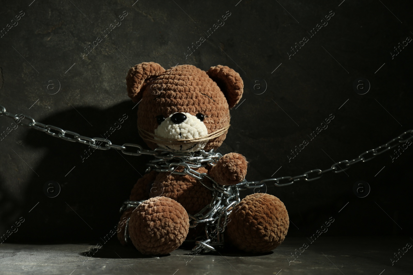 Photo of Stop child abuse. Chained toy bear on dark grey background