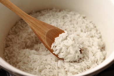 Pot with delicious rice and wooden spoon, closeup