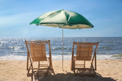 Photo of Green beach umbrella and deck chairs on sandy seashore