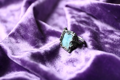 Photo of Beautiful silver ring with larimar gemstone on violet fabric. Space for text