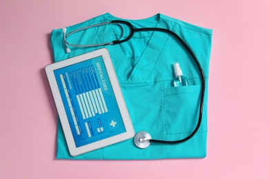 Photo of Medical uniform, stethoscope and tablet on light pink background, flat lay