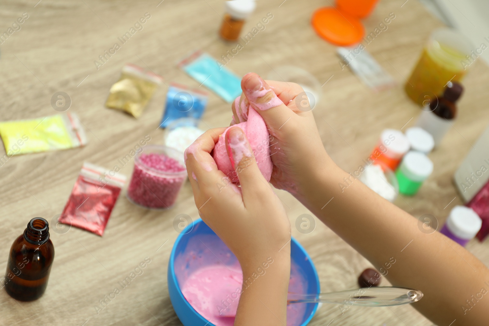 Photo of Little girl making DIY slime toy at table, closeup