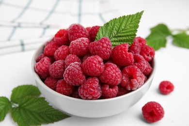 Photo of Bowl of fresh ripe raspberries with green leaves on white table