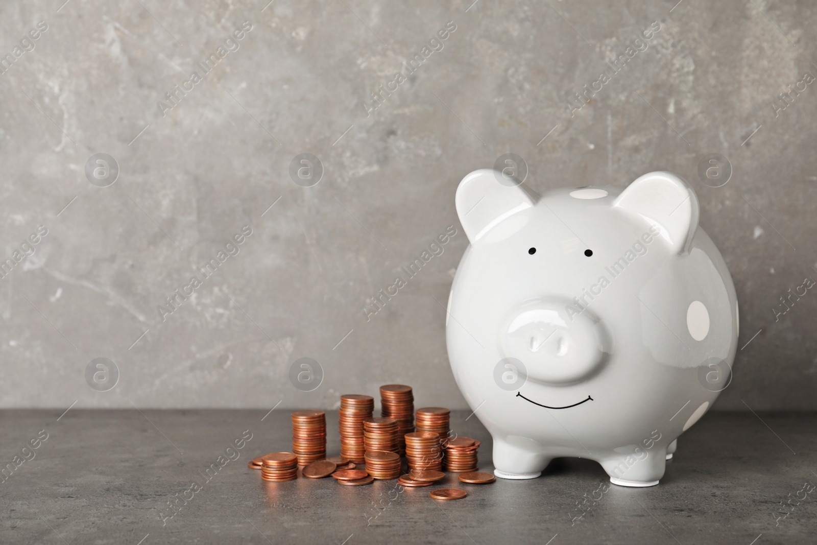 Photo of Ceramic piggy bank and many coins on table against grey background. Space for text