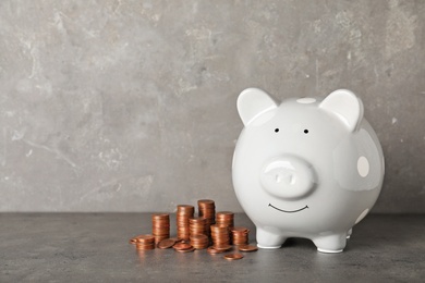 Photo of Ceramic piggy bank and many coins on table against grey background. Space for text